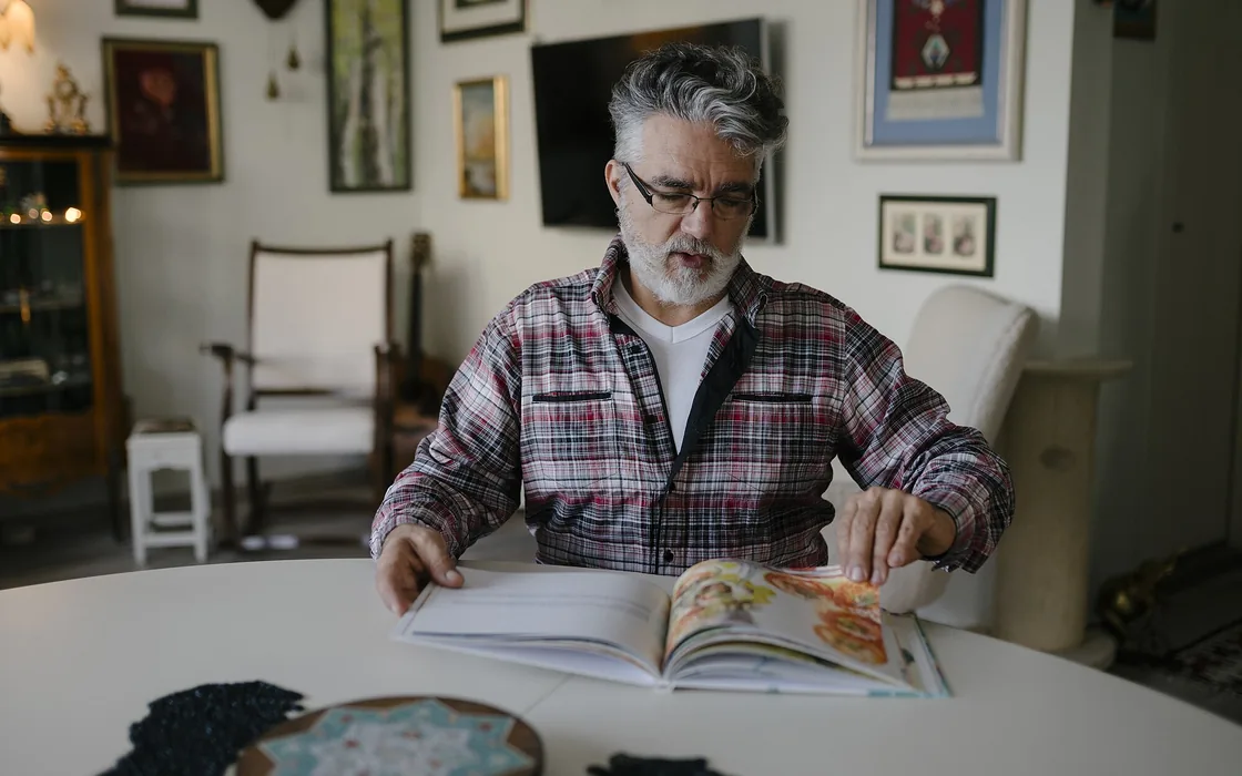 A man in his sixties sitting at a table at home, reading, in soft daylight.