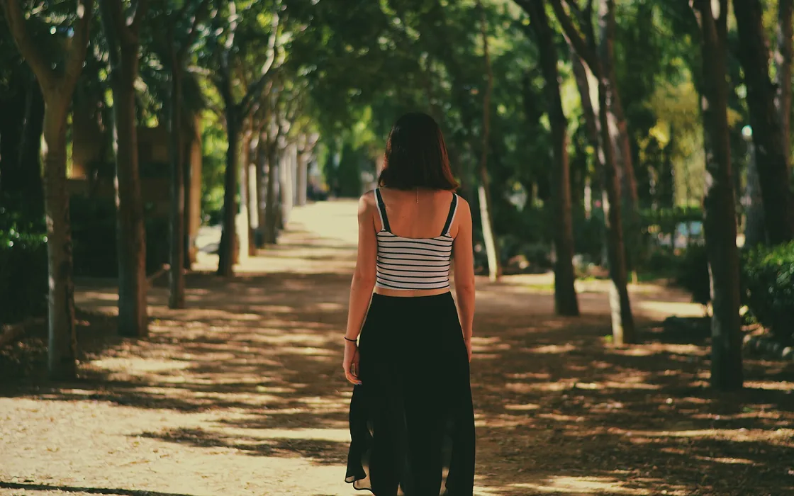 A woman walking away along a tree-lined path in dappled afternoon light.