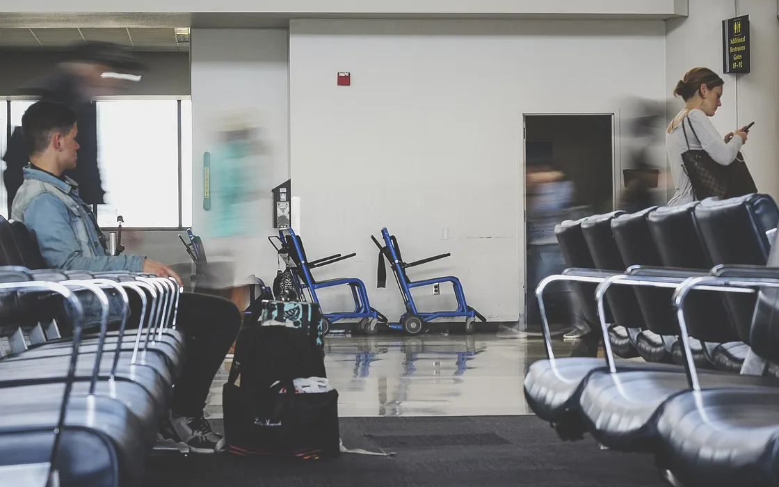 A bright hospital waiting area with rows of empty chairs and two people passing through.